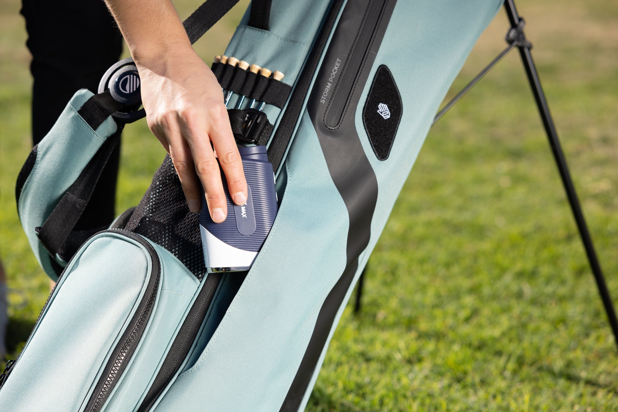 woman putting range finder into seafoam green El Camino golf bag by Sunday Golf
