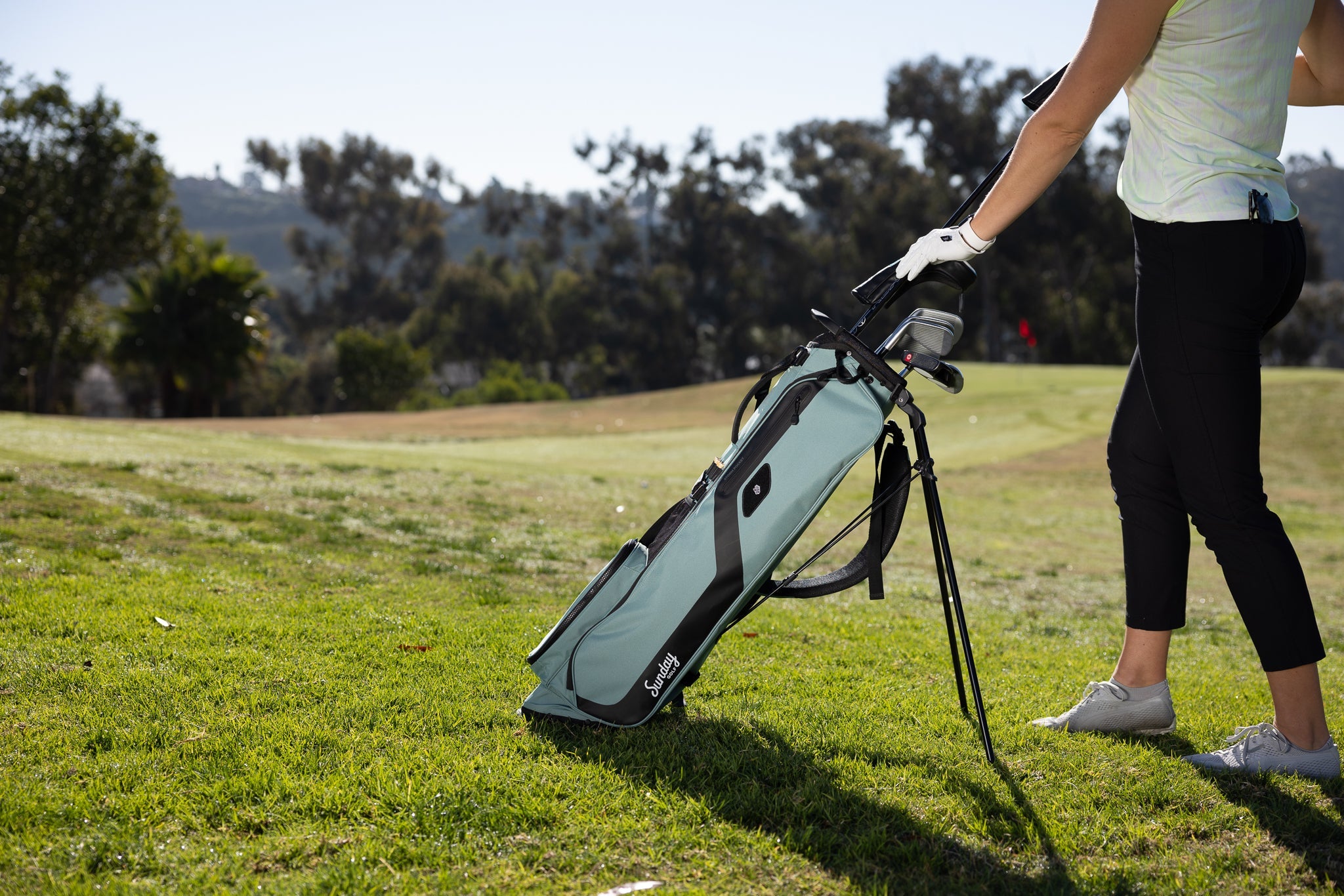 woman putting clubs in the seafoam green El Camino golf bag by Sunday Golf 