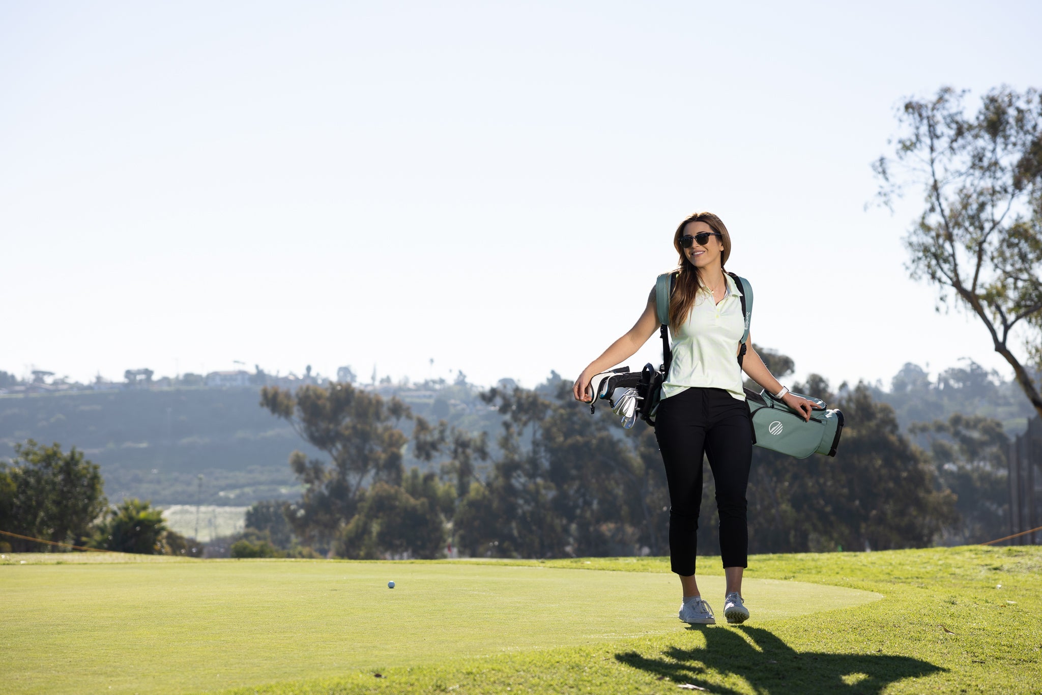 woman smiling, carrying seafoam green El Camino golf bag by Sunday Golf