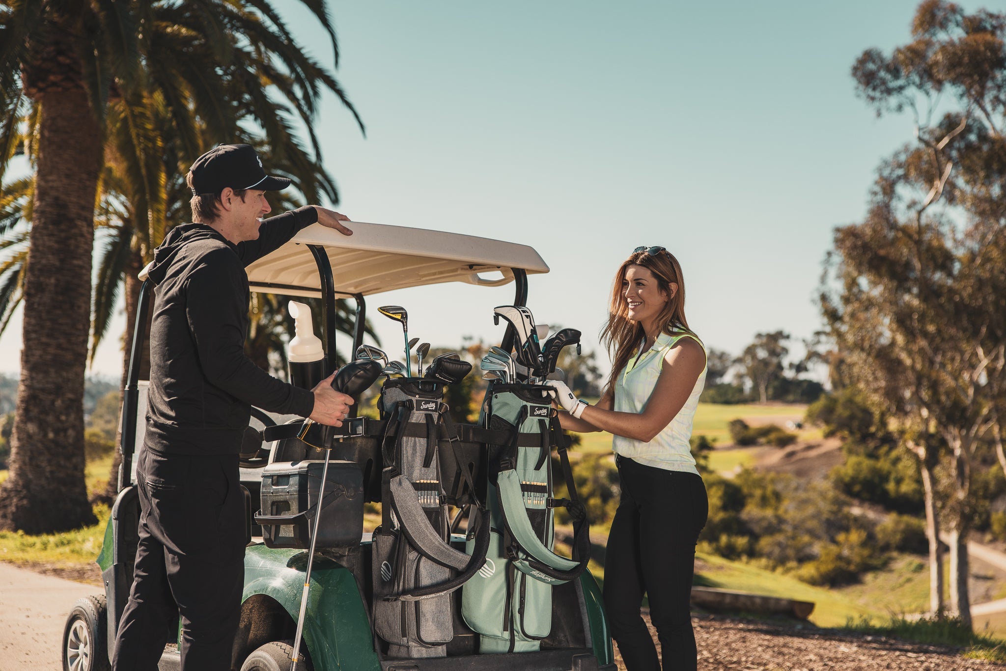 man with heather gray El Camino golf bag by Sunday Golf and woman with seafoam El Camino golf bag by Sunday Golf on a golf cart